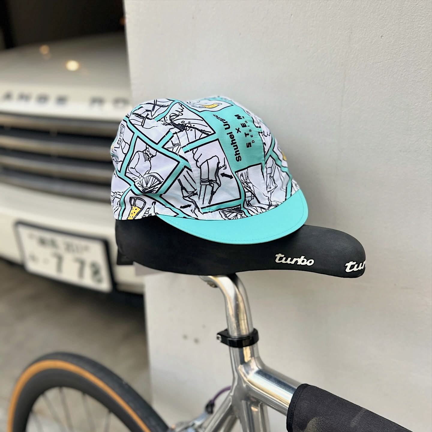 STEM DESIGNと浦野周平のコラボ商品第三弾となるサイクルキャップ。ターコイズブルーのプリントの中に「自転車乗車後の点検」イラストがレイアウトされています。